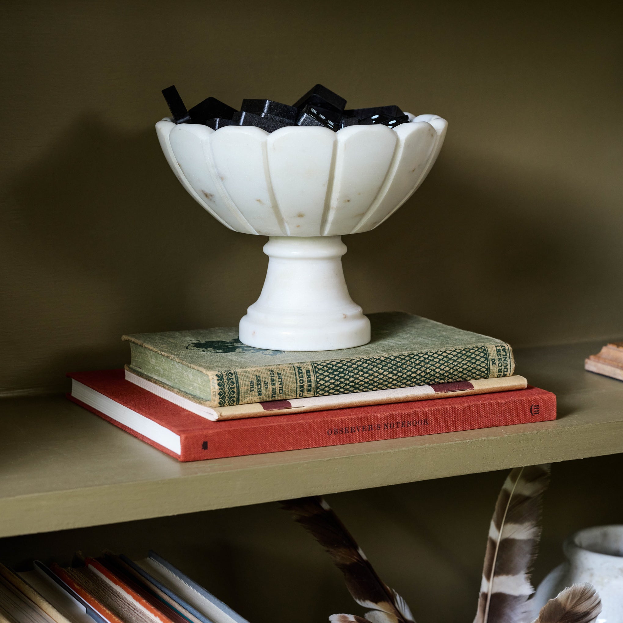 Marble Scalloped Accent Bowl containing dominoes on a bookshelf