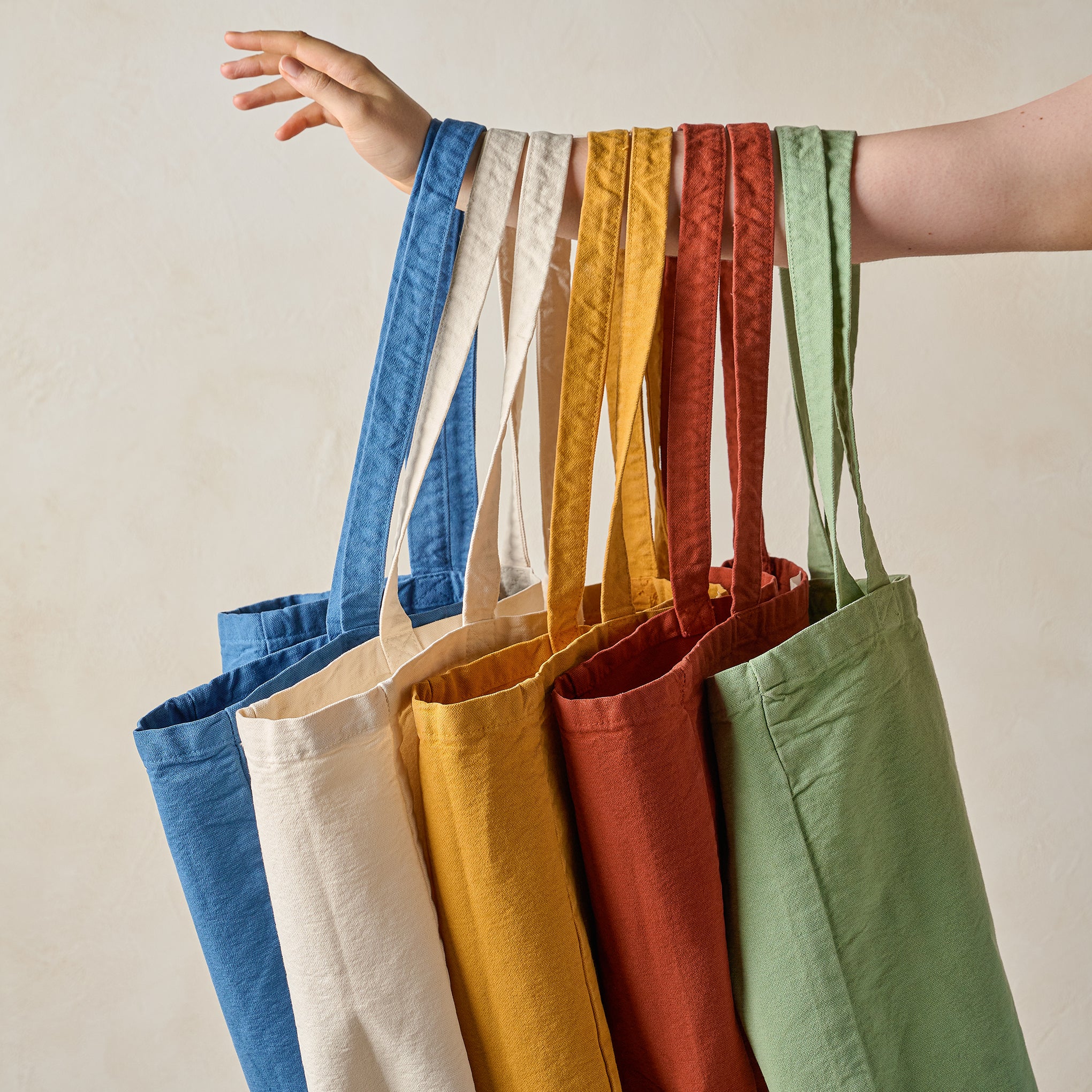 Magnoliass Seafoam Script Tote an arm holds various colors of the Magnoliass tote