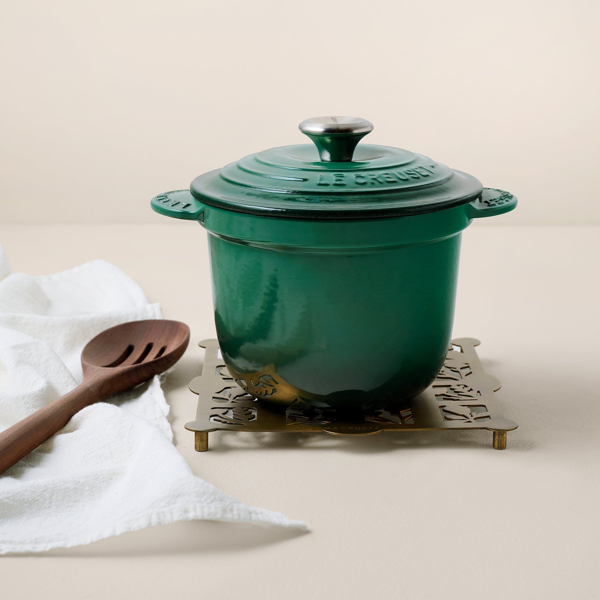 Antique Brass Shadow Floral Trivet shown with dutch oven, tea towel, and slotted spoon