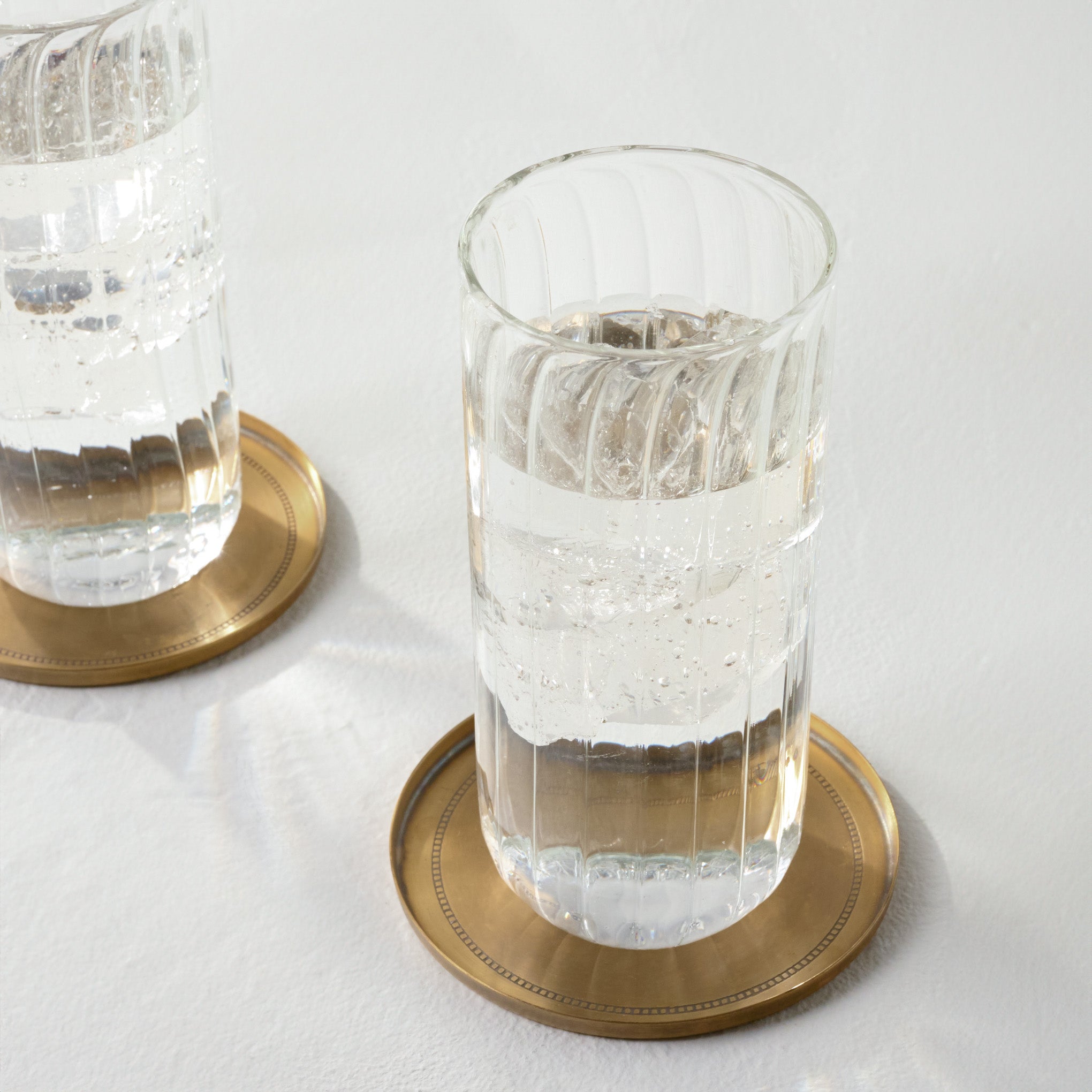 Magnoliass Etched Brass Coaster Set of Four shown with tumbler glass