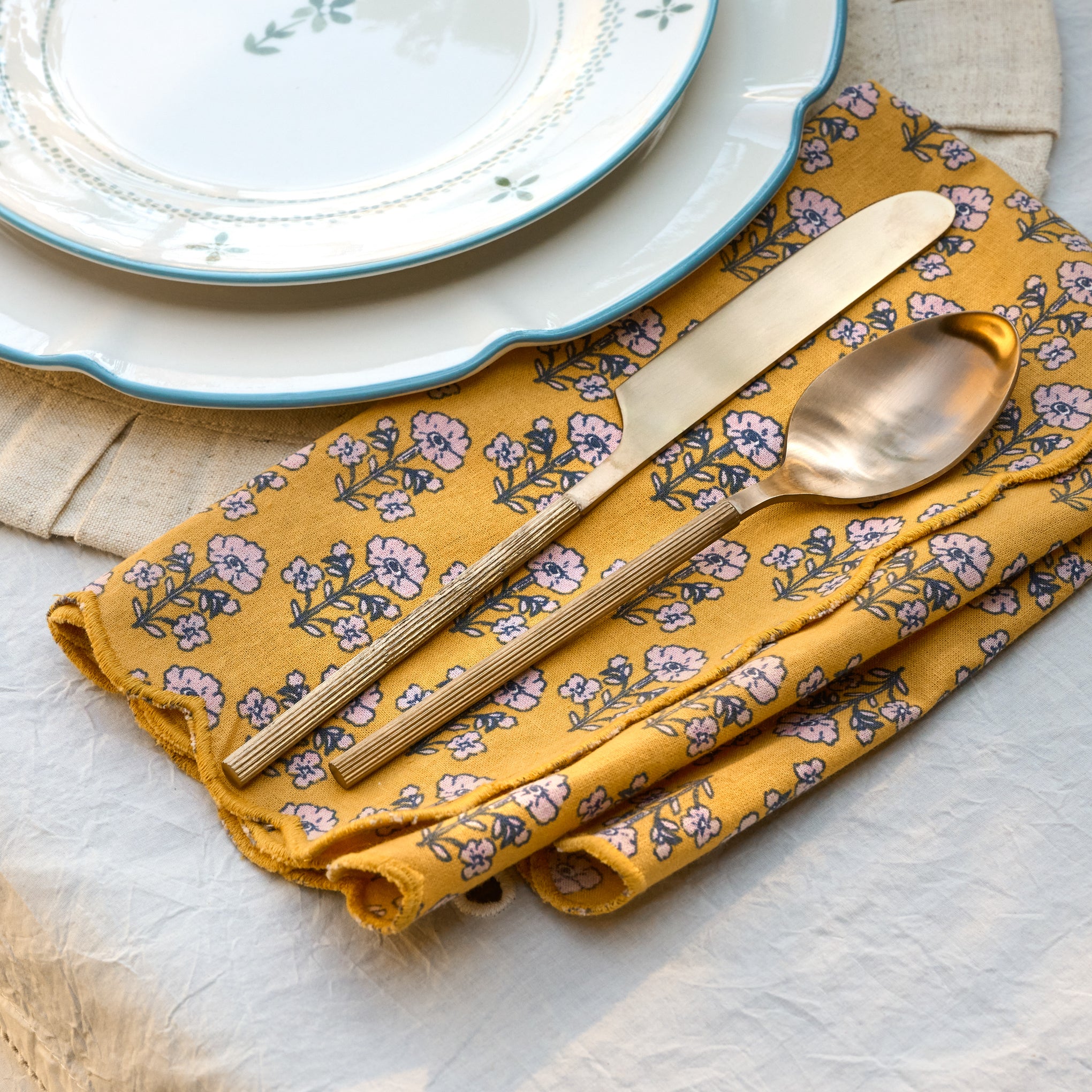 Maize Scallop Edge Block Print Napkin Set shown on table with ribbed silverware and luna plates