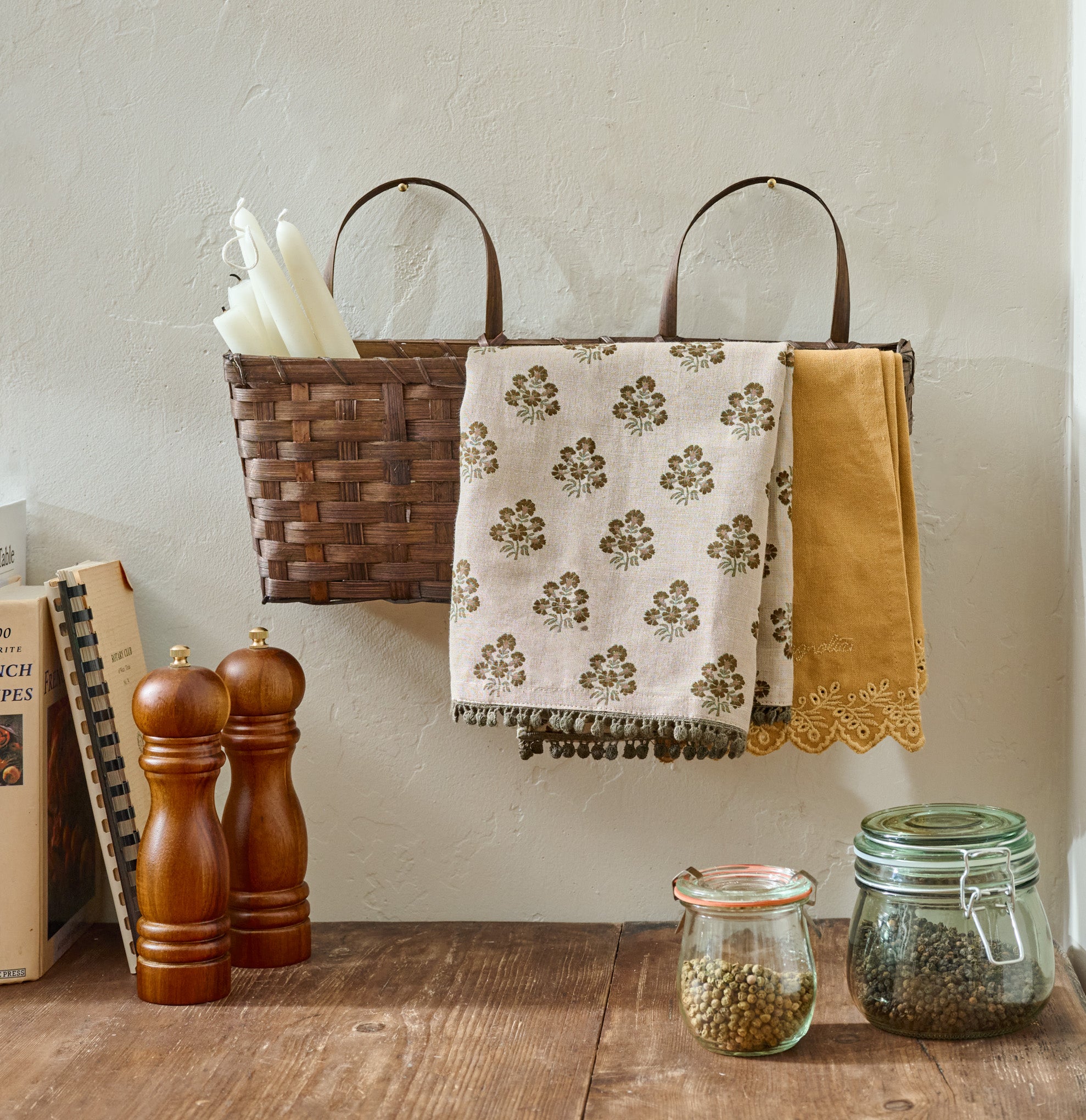 Small Damian Woven Wall Basket shown hung on wall holding towels and taper candles