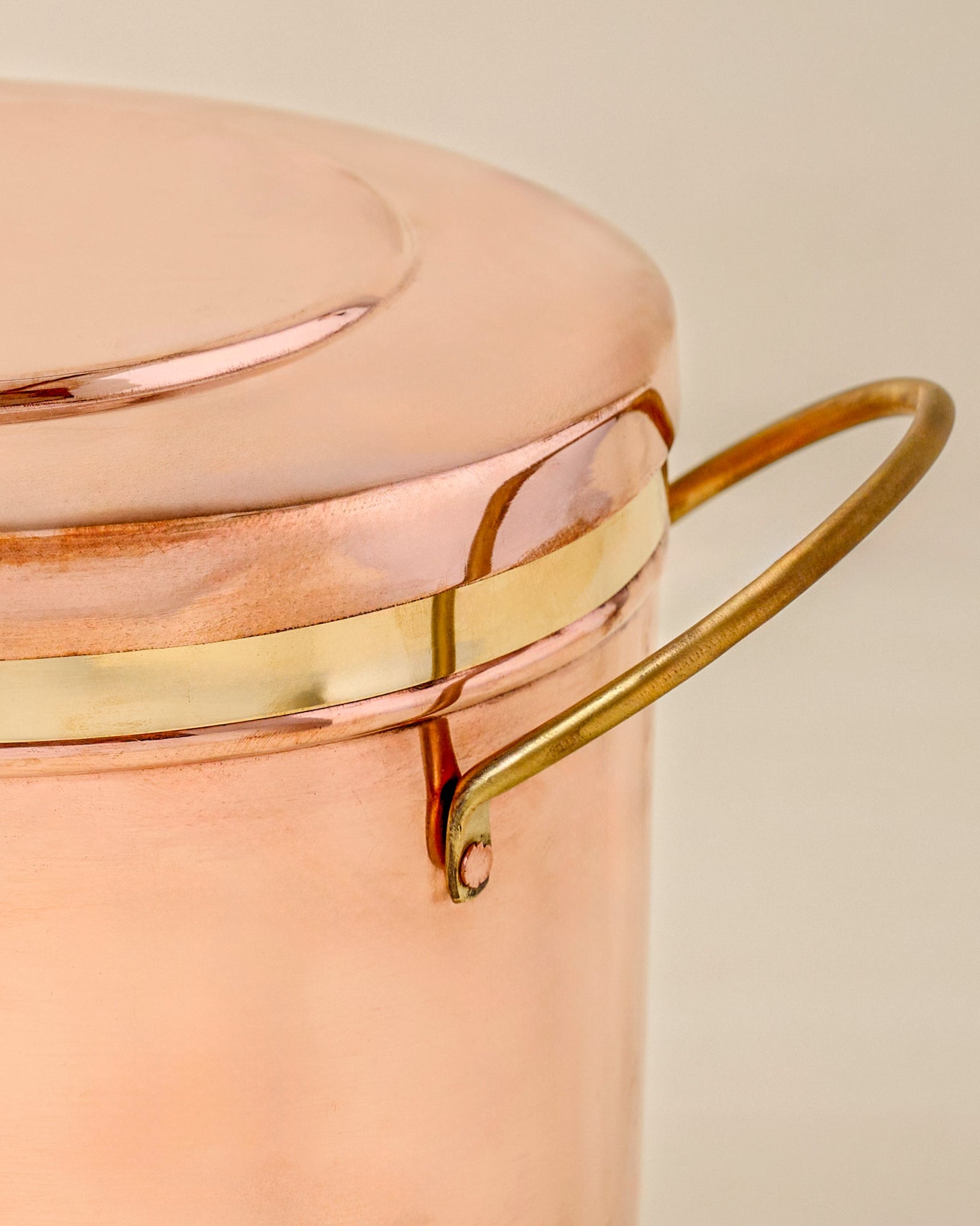 Close-up of a copper bread box with brass handle and trim on a beige background
