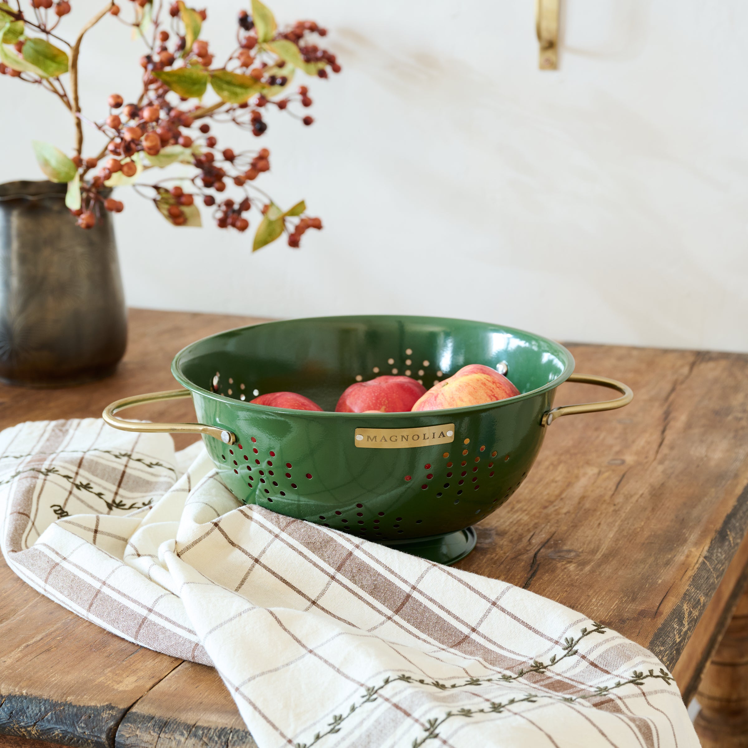 Magnoliass Laurel Green Colander shown with fruit and tea towel