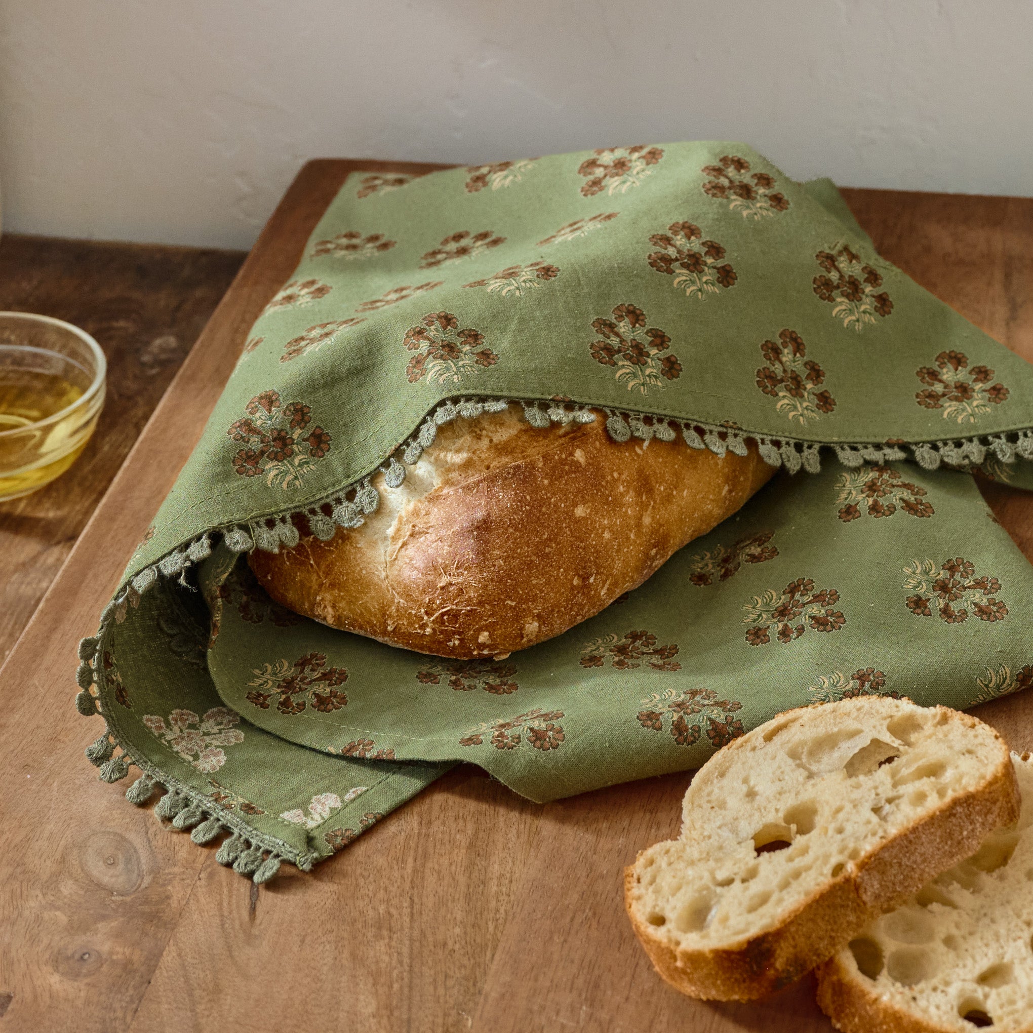 Magnoliass Olive Green Block Printed Tea Towel shown wrapping bread