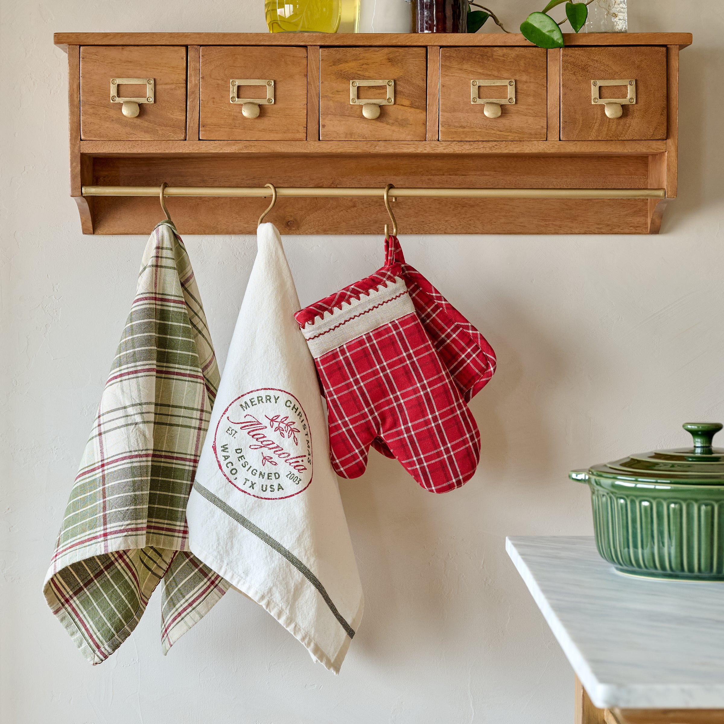 Magnoliass Vintage Red Plaid Oven Mitt and Pot Holder Set shown hung on cole wooden wall cabinet with rail