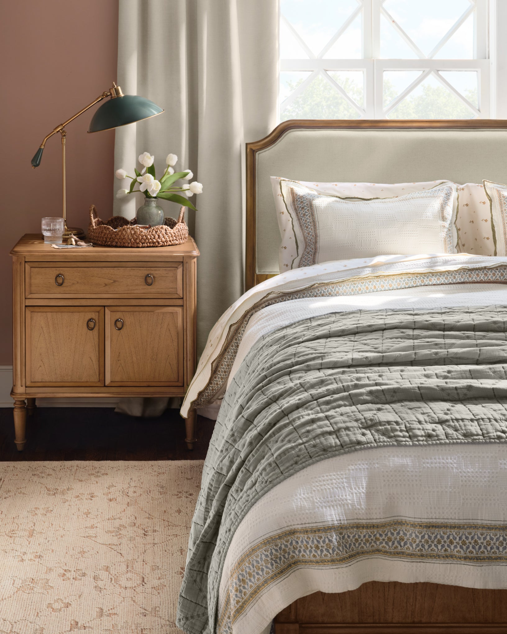 Bedroom with wooden nightstand, bed with patterned bedding, and lamp.