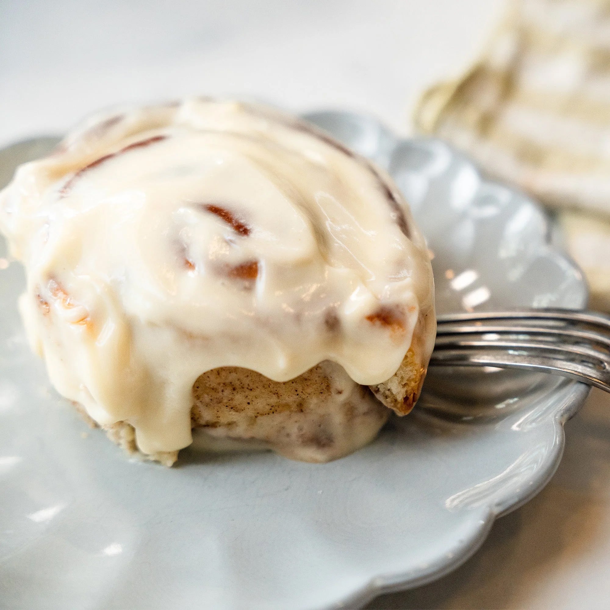 Cinnamon roll with cream cheese frosting on a white plate with a fork.