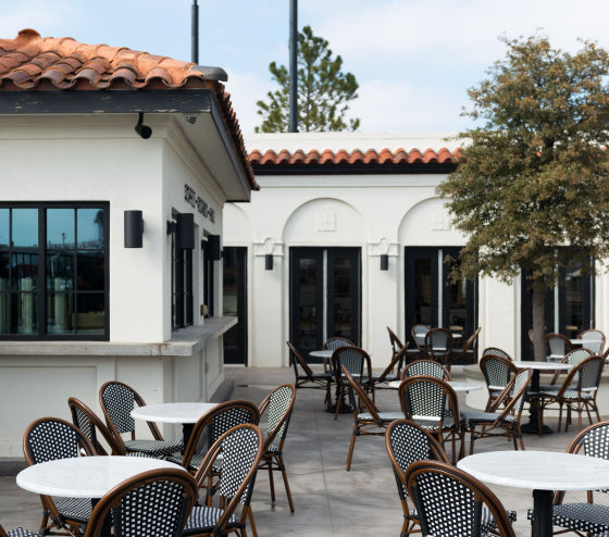 Outdoor seating area with tables and chairs in front of a Magnoliass Table restaurant with red tile roof.