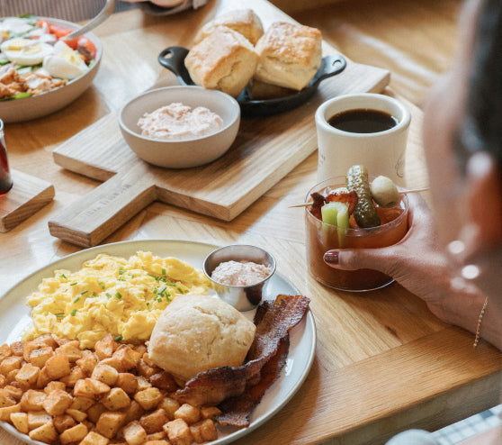 Breakfast spread with eggs, bacon, biscuits, and coffee on a wooden table.