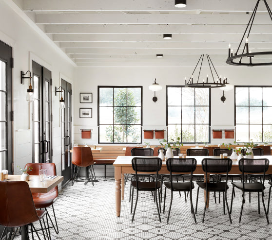 Modern dining room with wooden tables and chairs, large windows, and white walls.