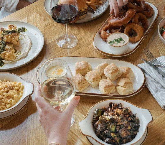Dinner table with various dishes including bread, macaroni and cheese, and a glass of white wine.