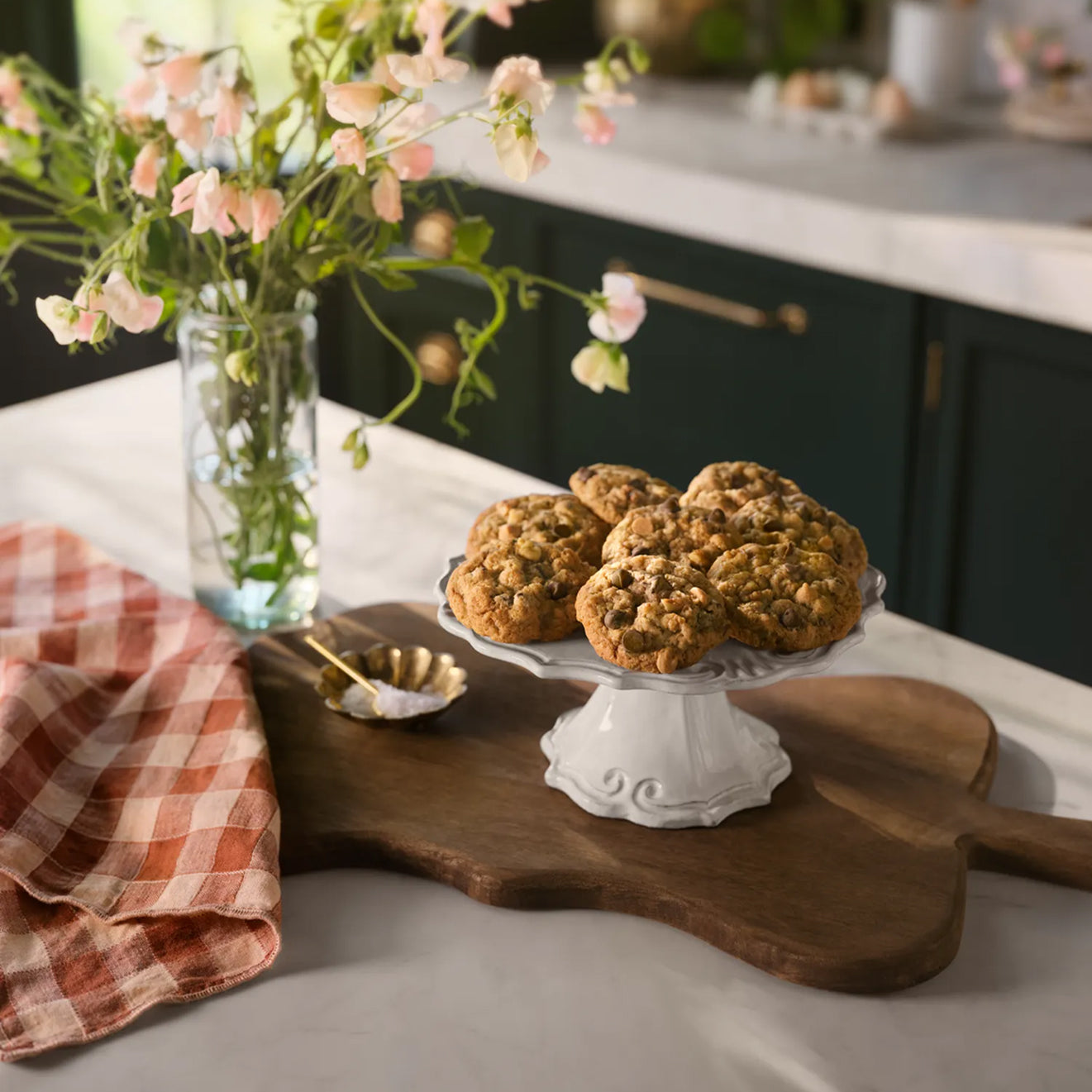 Baked Magnoliass Table Silo Cookies on a white cake stand with flowers and a checkered cloth in the background.