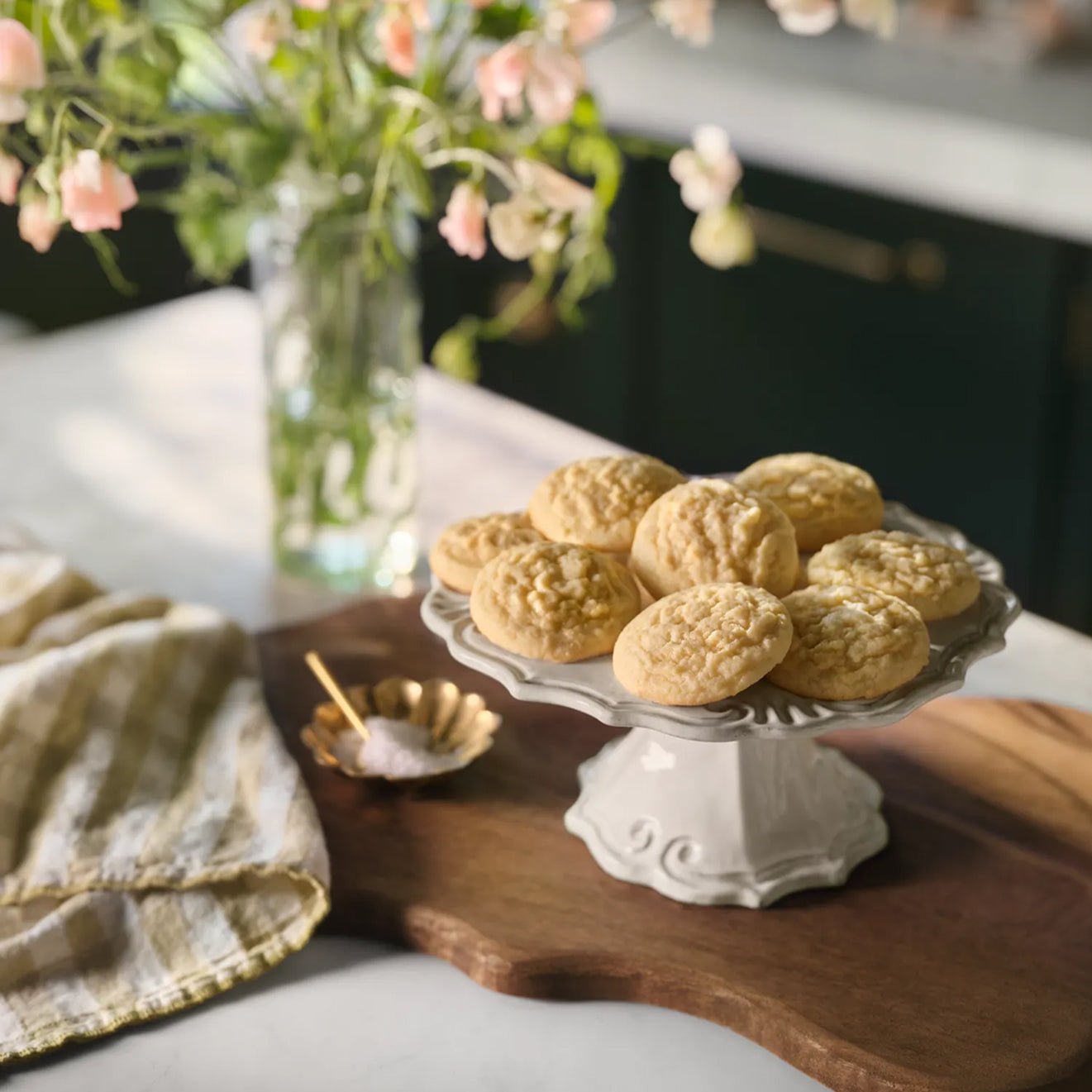 Decorative plate of Magnoliass Table Classic Sugar Cookies on a wooden tray with flowers in the background.