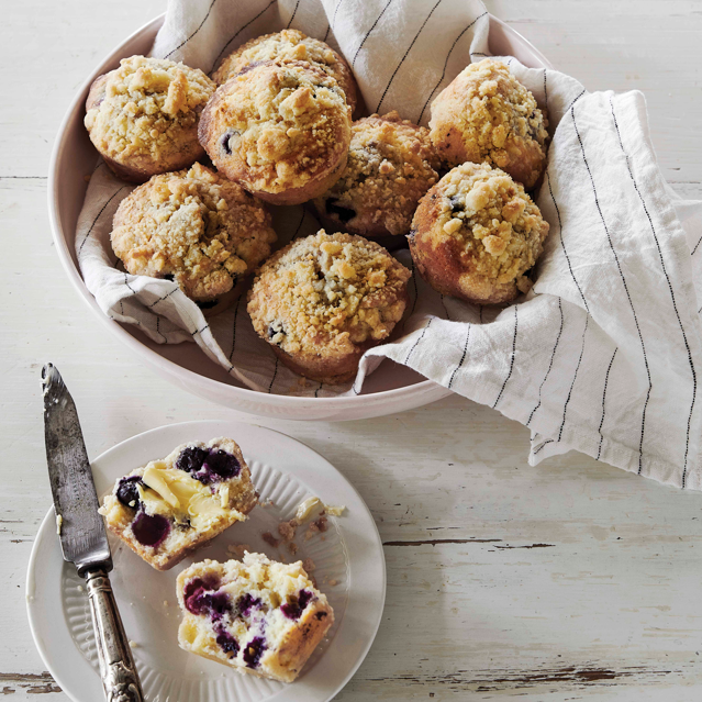 Muffins in a bowl with one cut open on a plate on a wooden surface.