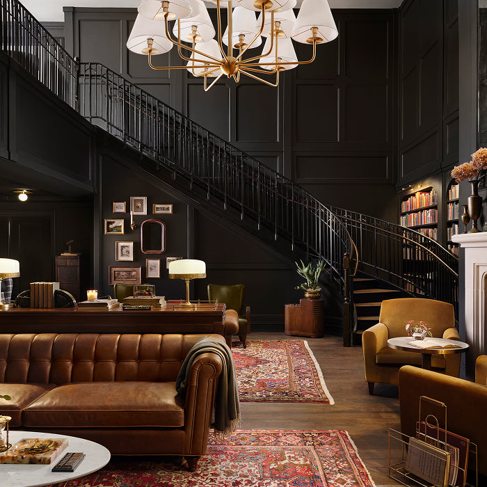 I room shot of the library at Hotel 1928, a luxurious interior with a staircase, chandelier, and brown sofa.