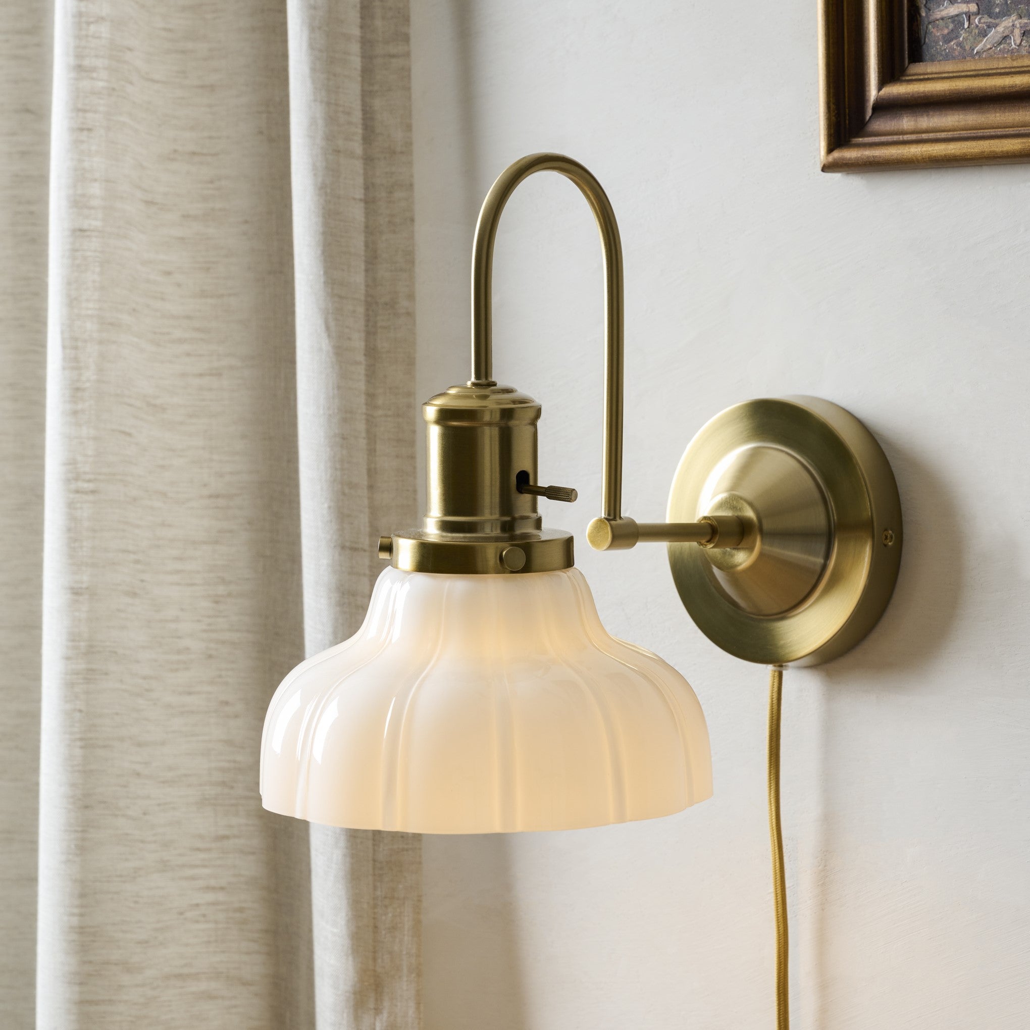 Wall-mounted brass lamp with a white glass shade on a neutral wall.