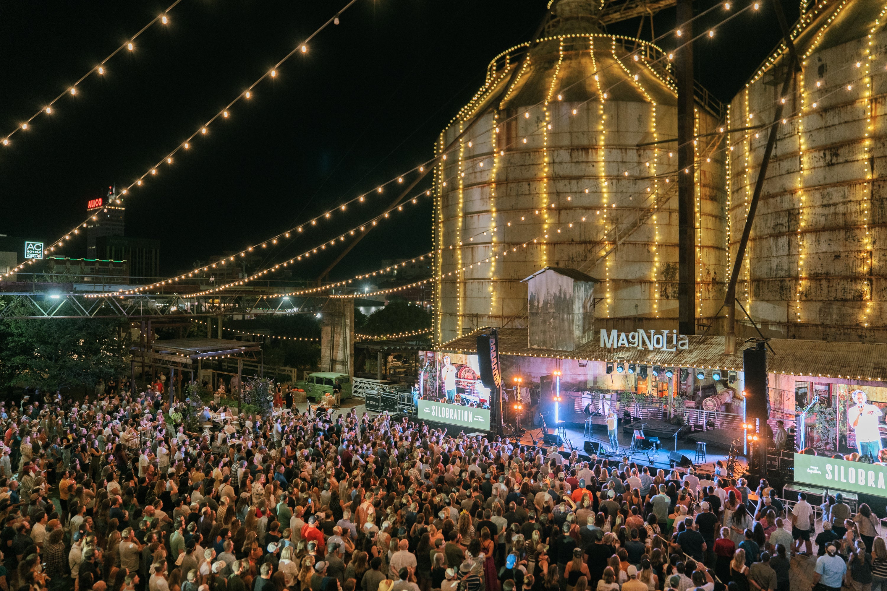 Large crowd gathered at a concert event under a large industrial silo structure with lights.  Learn more about Silobration at Magnoliass.