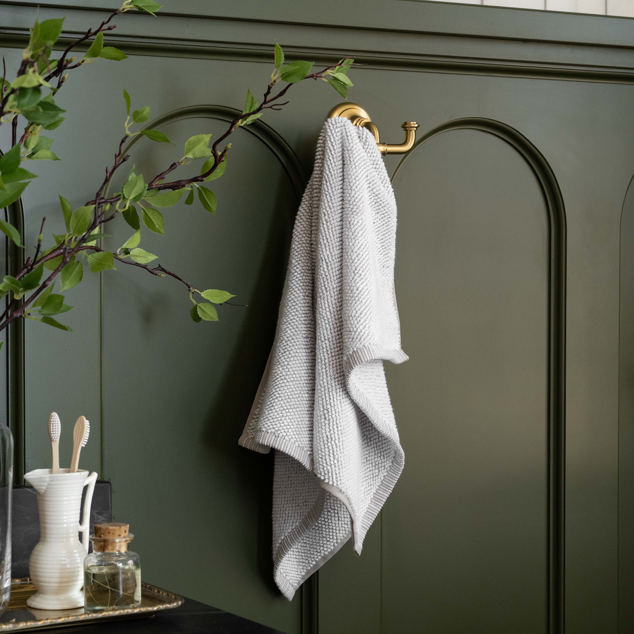 Linen Assisi Textured Towel hanging on gold wall hook against green wainscoting 