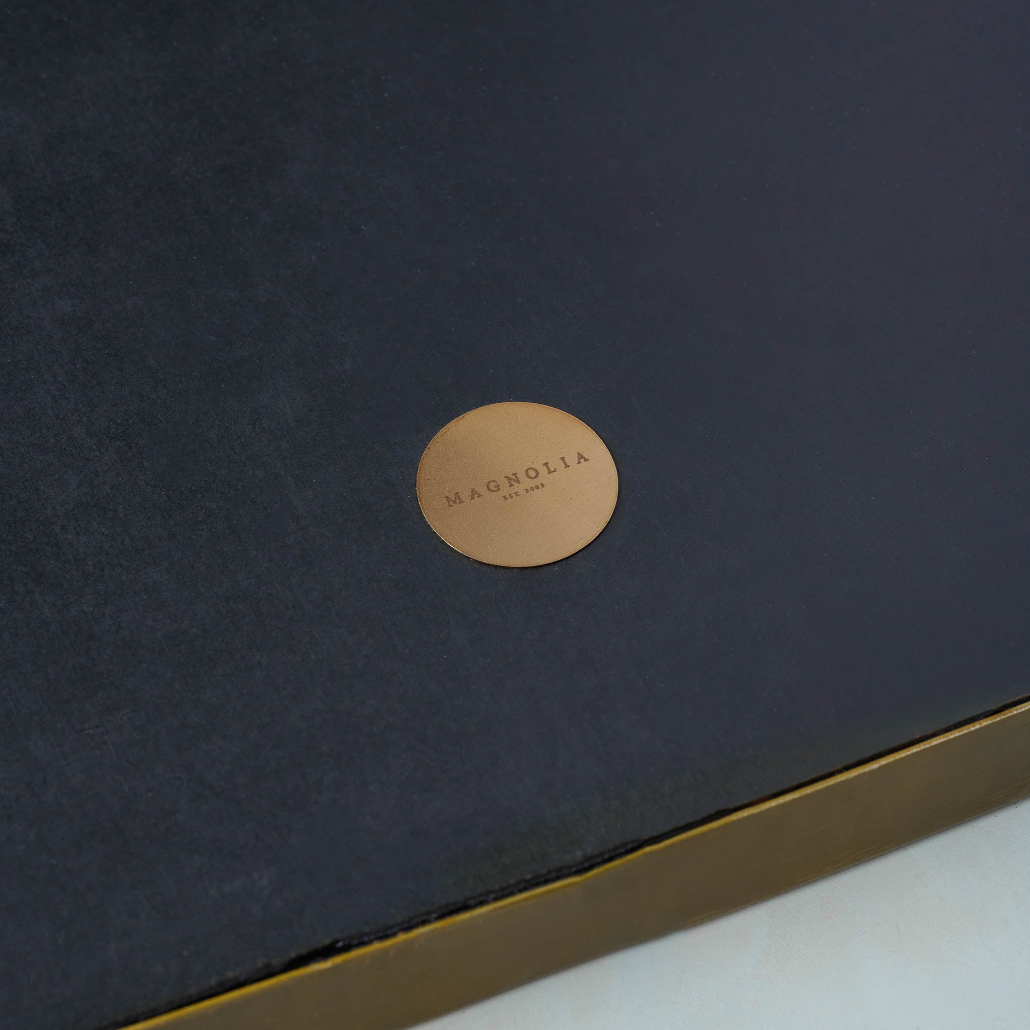 Close up of gold Magnoliass circle logo on back of Dorian Brass Mantle Mirror