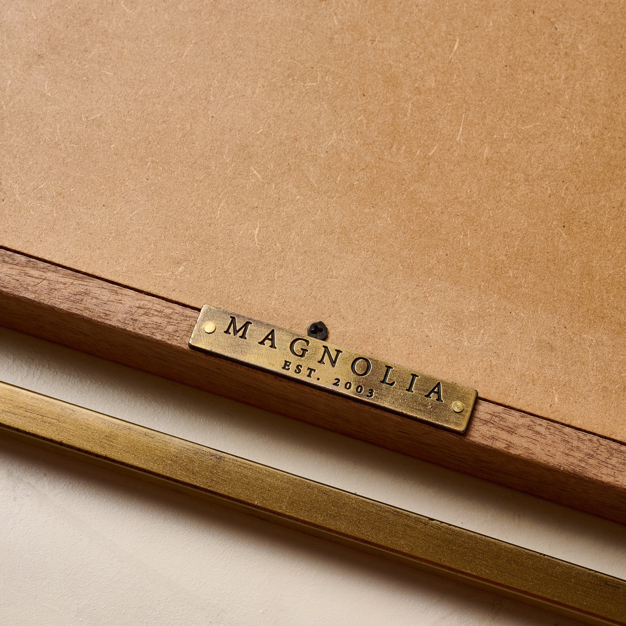 Close up of metallic Magnoliass logo tag on back of Flora Rectangle Mirror