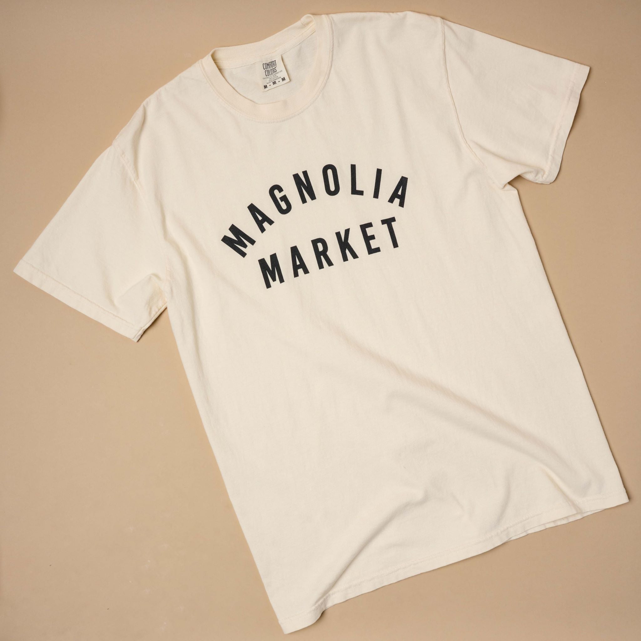 Top view of Magnoliass market ivory shirt that reads Magnoliass Market in plain black text.
