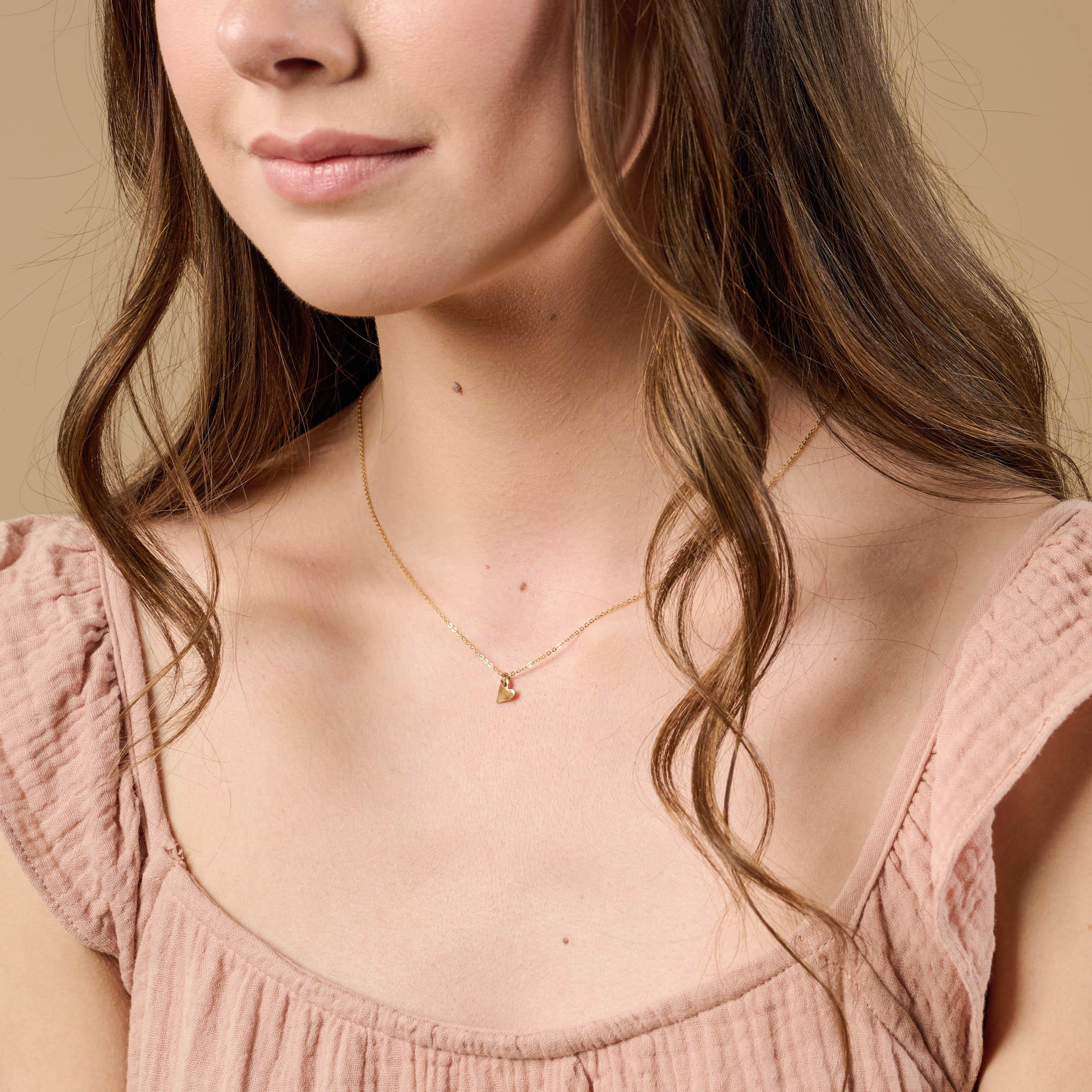 small gold heart charm on gold chain on model. 