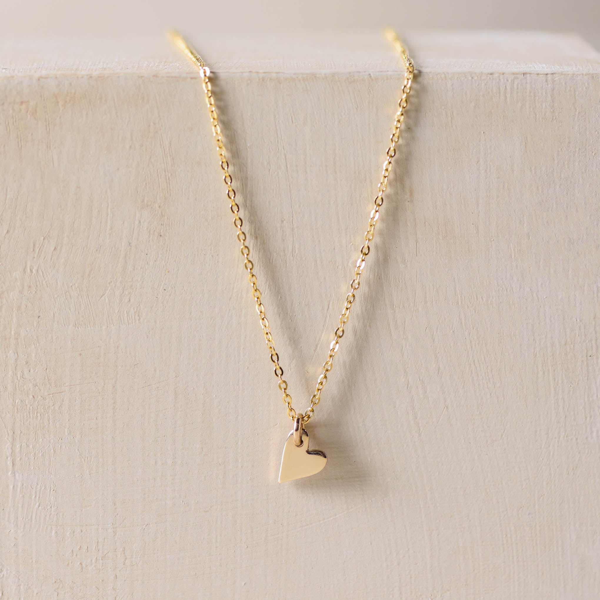 gold small heart charm on gold chain hanging down a backdrop. 
