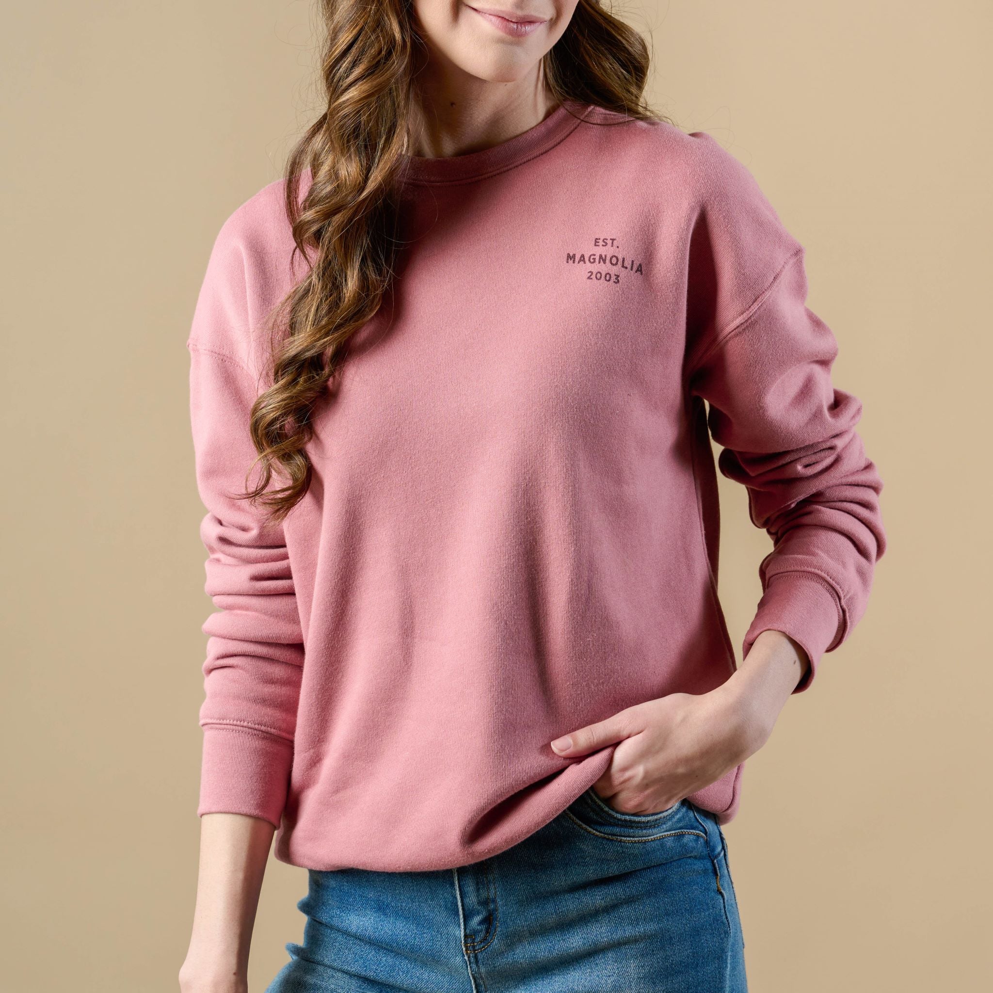 Sweatshirt in mauve color on model. Small text on front of sweatshirt, upper left chest reads Est. Magnoliass 2003. Text color is maroon.