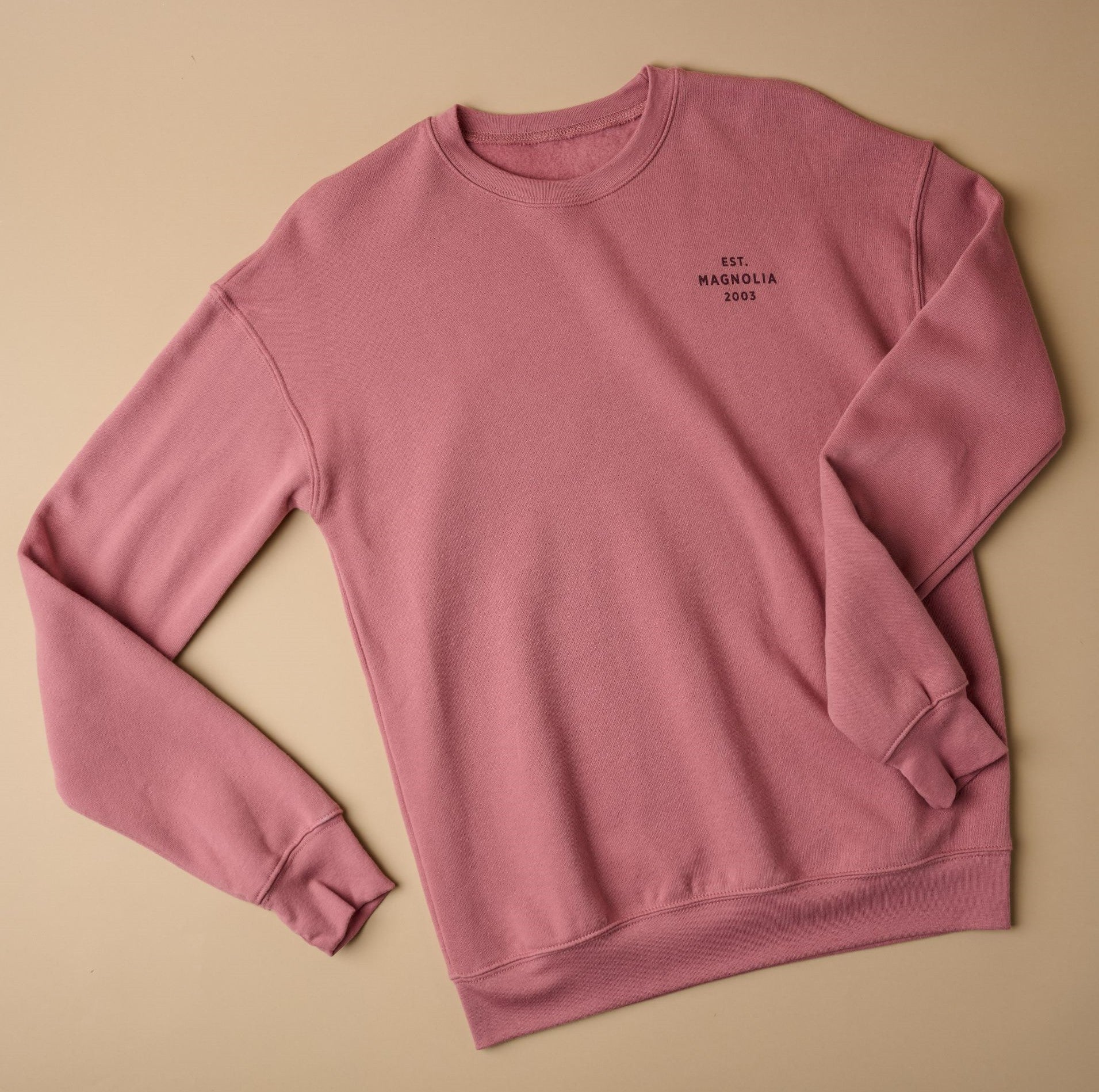 Top view of mauve sweatshirt that reads EST Magnoliass 2003 on left chest in plain font, all capital letters. Text color is maroon. 