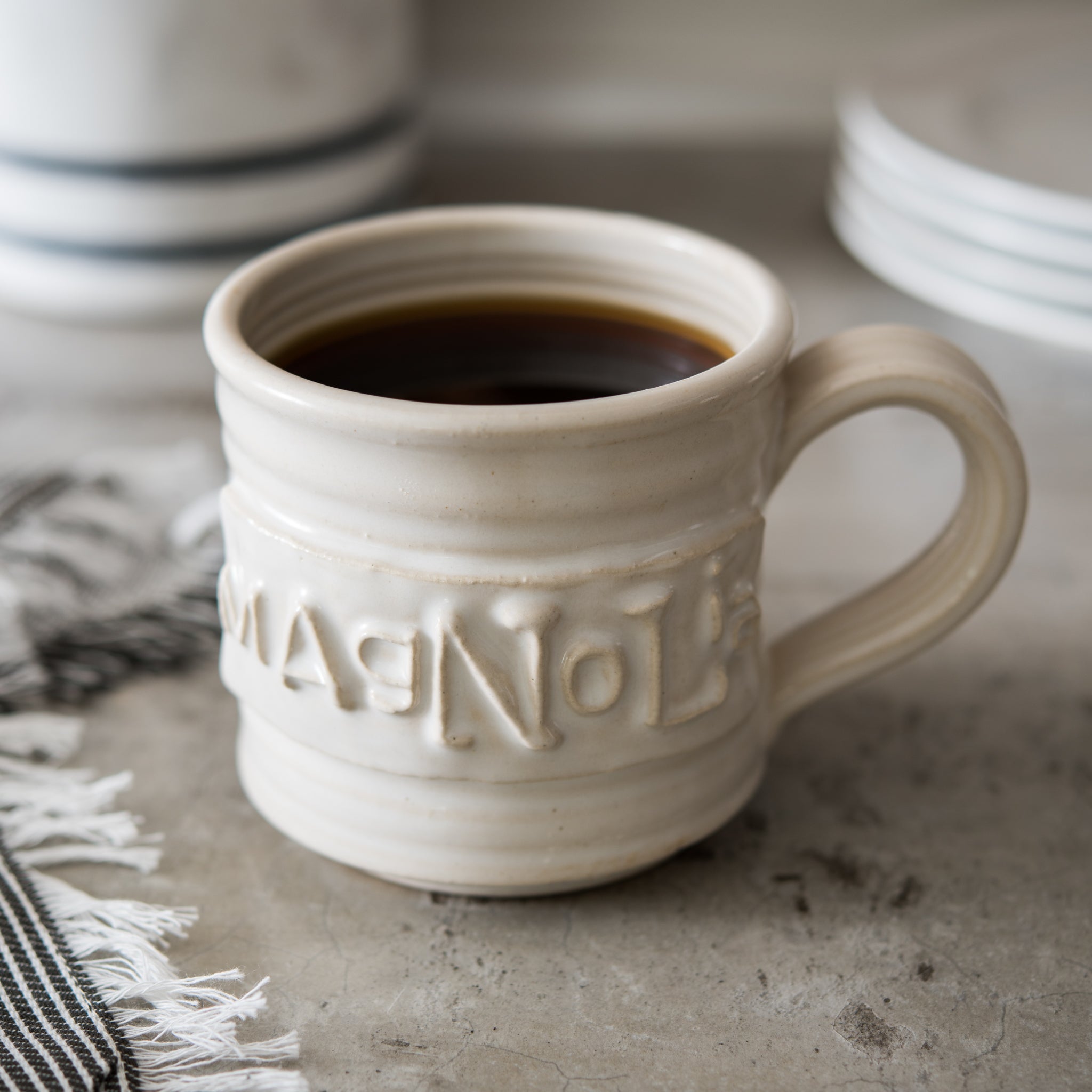 white handthrown ceramic mug with original Magnoliass logo embossed on side