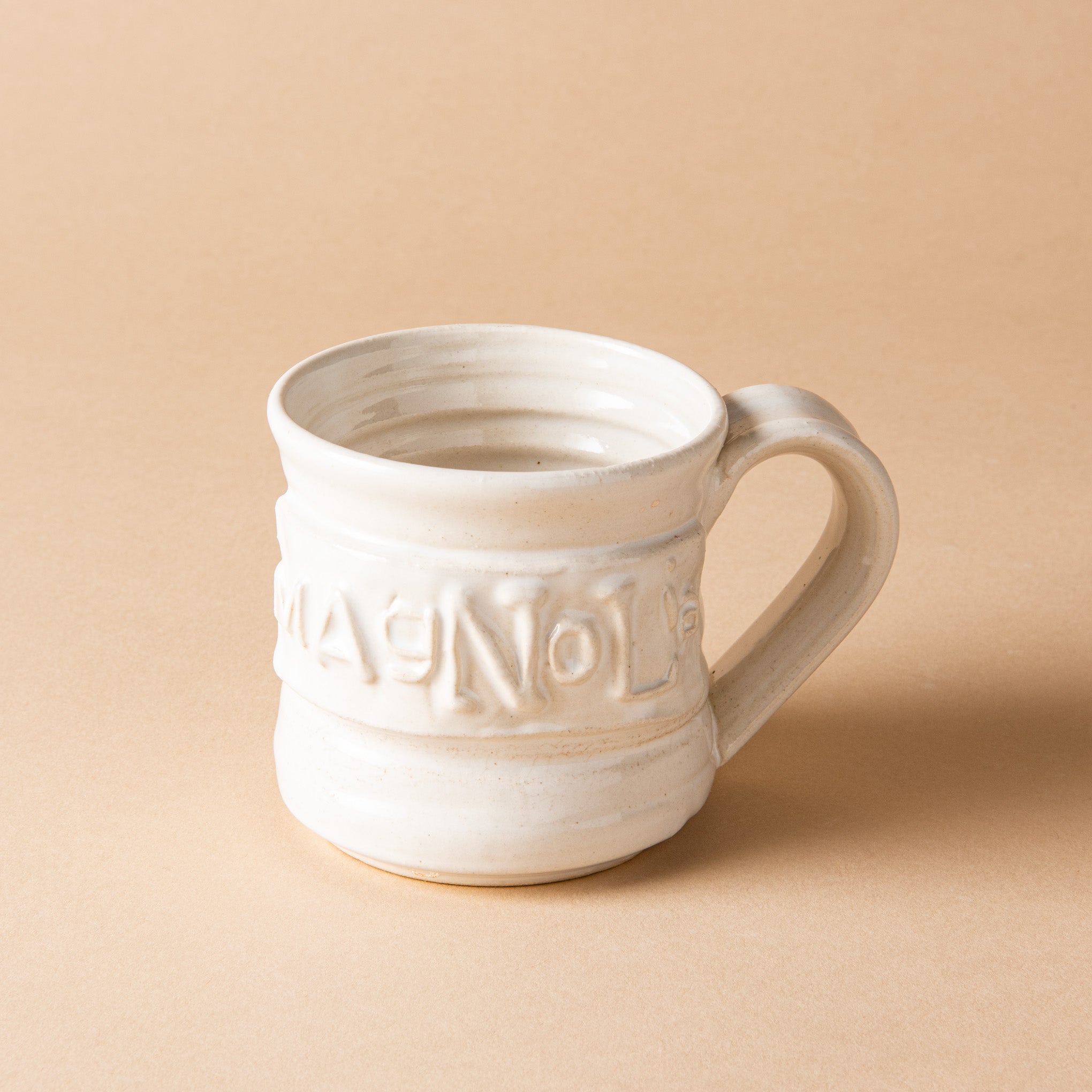 white handthrown ceramic mug with original Magnoliass logo embossed on side